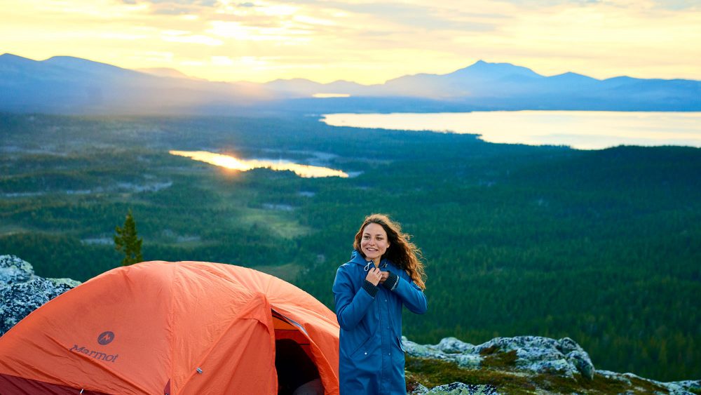 Pretty girl stands by her tent on a hill in Norway