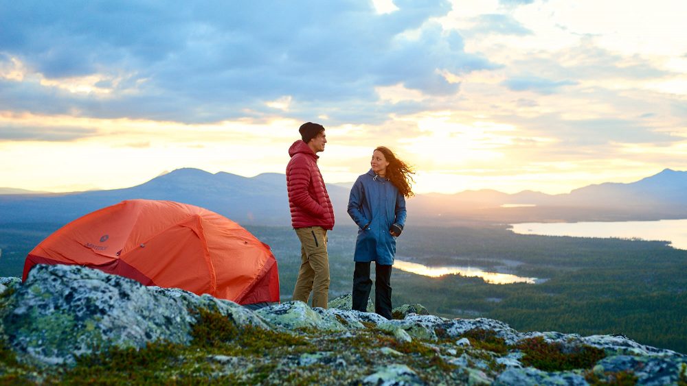 Couple enjoy an epic sunset by their tent on a hill in Norway