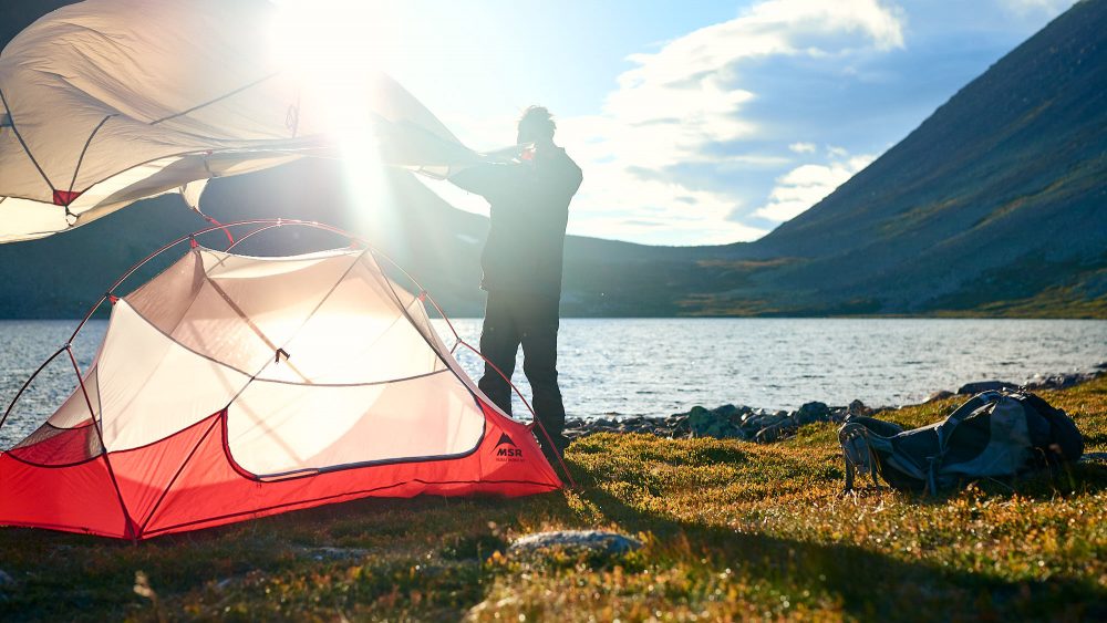 Hiker setting up his tent by a mountain lake in Norway