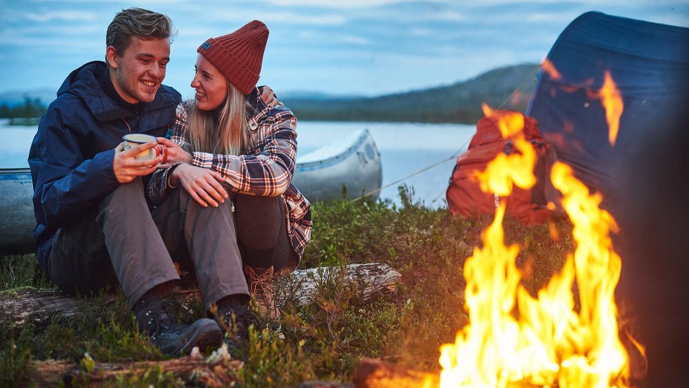 Couple sitting by a campfire with their canoe in Norway