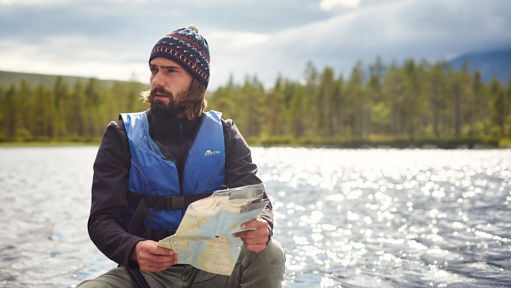 Bearded man reading a map in a canoe on a lake in Norway