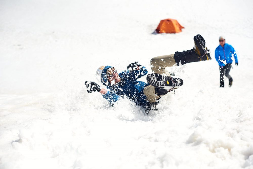 Alpinist doing a training drill, sliding down a hill, trying to stop his fall with an ice axe